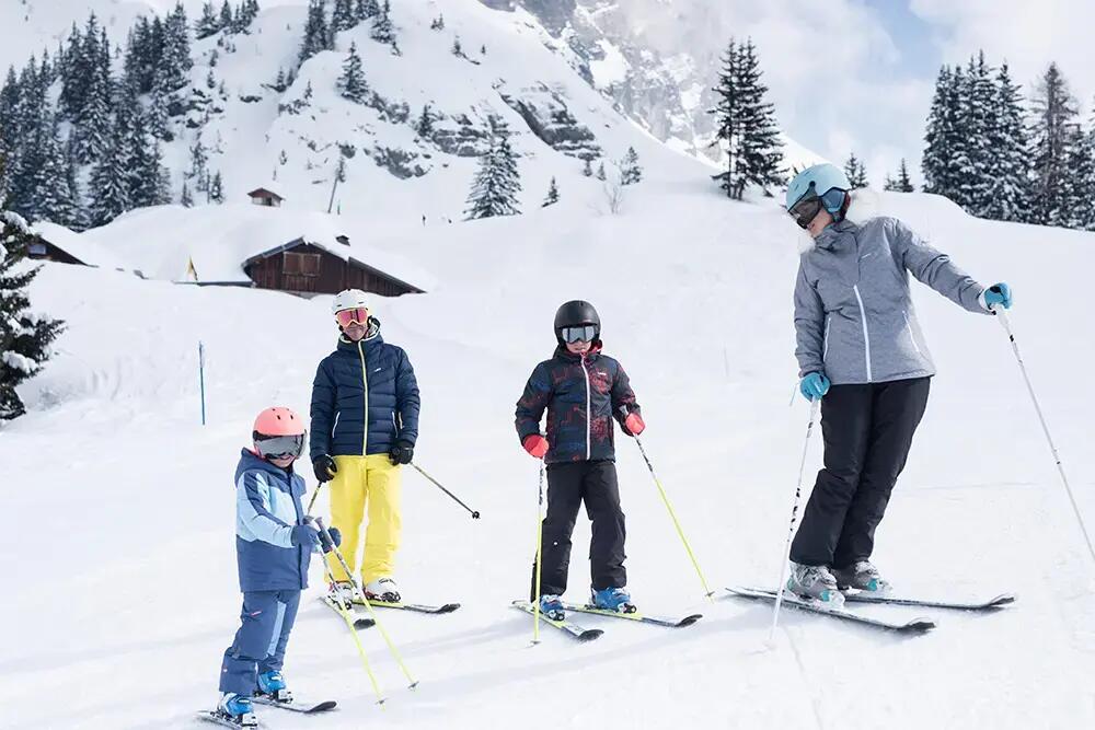 rodzina ubrana w odzież sportową z nartami, kijkami, kaskami i goglami na stoku narciarskim