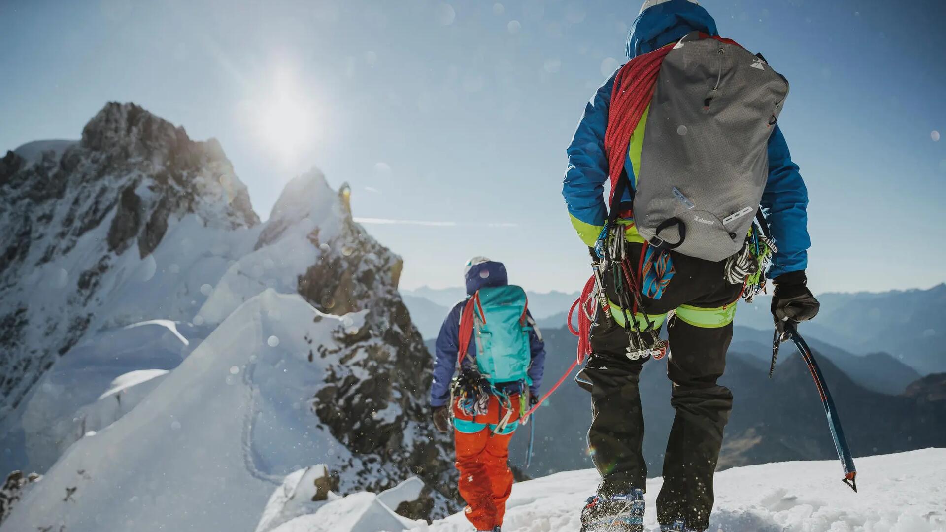 osoby w strojach alpinistycznych z uprzężami i plecakami wędrujący po górach