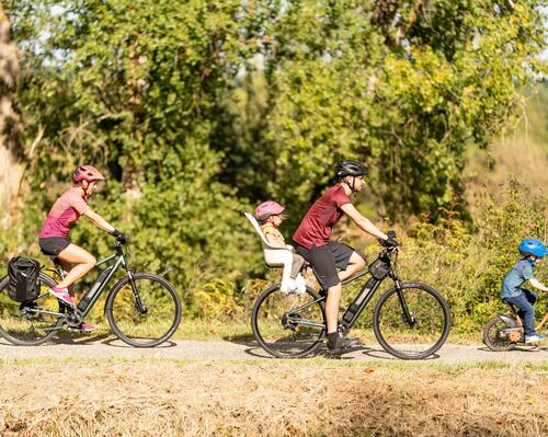 Rodzina w strojach sportowych i kaskach jadąca leśną drogą na używanych rowerach elektrycznych