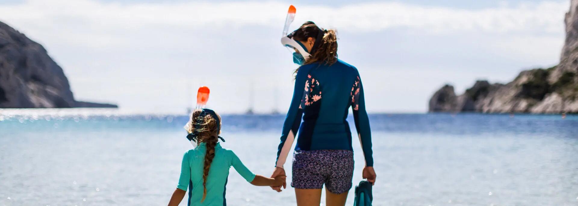 kobieta i dziewczynka idące do wody w strojach pływackich z maskami do snorkelingu i płetwami pływackimi