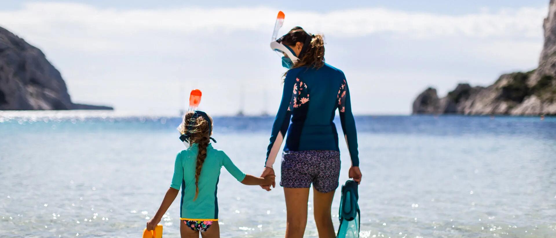 kobieta z dzieckiem w maskach do snorkelingu z płetwami pływackimi wchodzą do wody