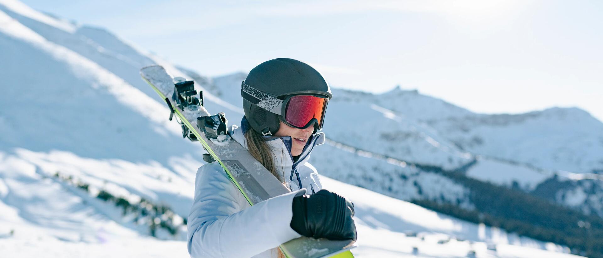kobieta w stroju narciarskim i goglach trzymająca narty na ramieniu