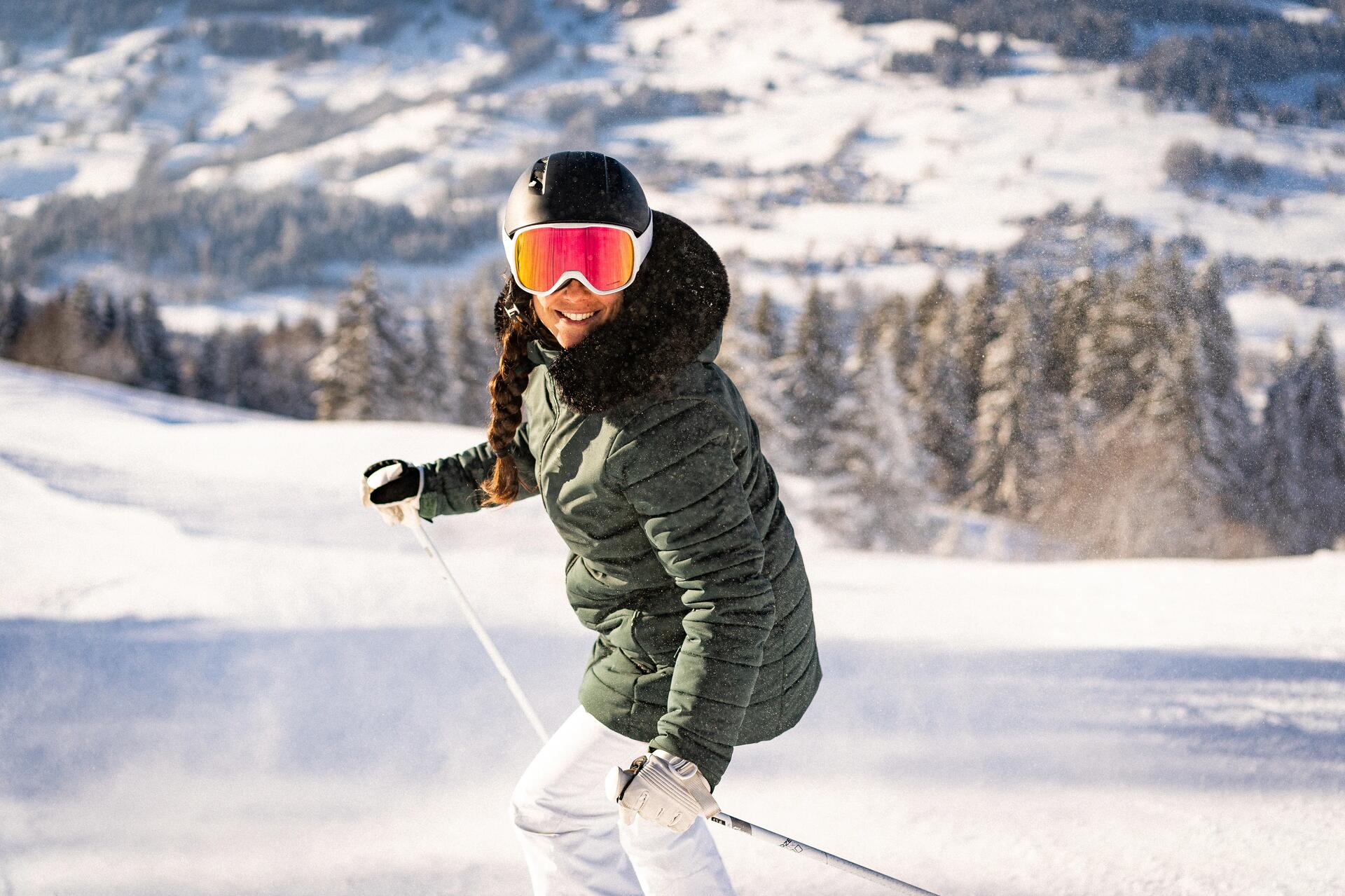 kobieta ubrana w kurtkę puchową w górach jeżdzi na nartach z kijkami