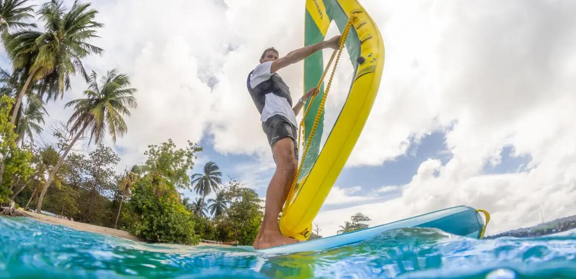 mężczyzna uczący się pływać na dmuchanej desce windsurfingowej