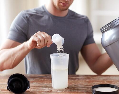 Guy pouring protein powder in to a protein shaker  
