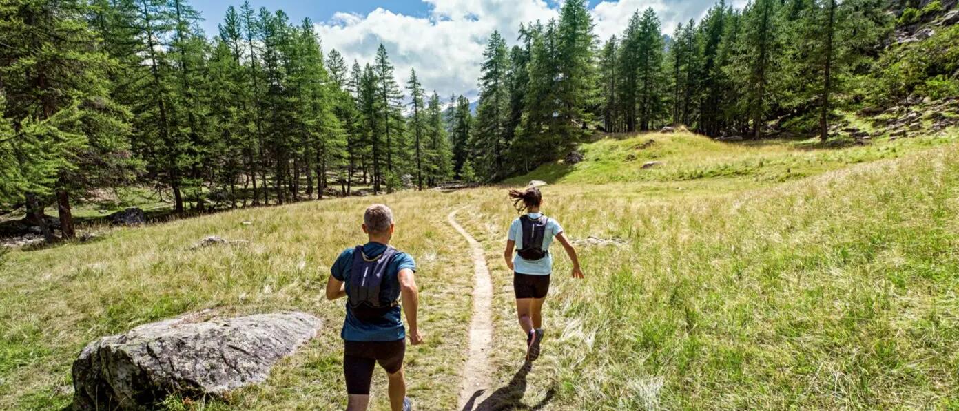 mężczyzna i kobieta biegnący w lesie z plecakami