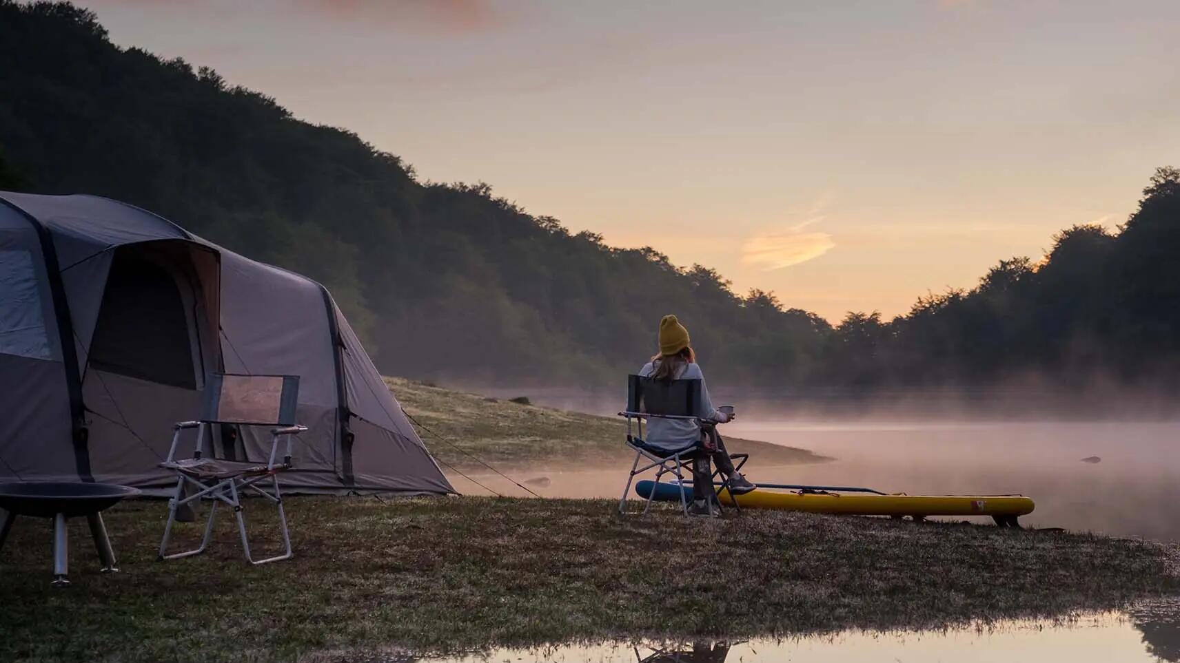 kobieta siedząca na krześle turystycznym przed namiotem nad jeziorem