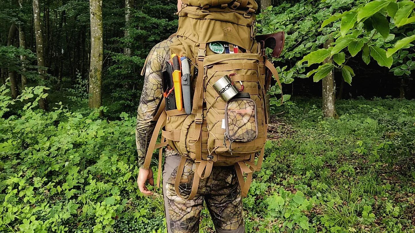 mężczyzna w stroju do uprawiania bushcraftu z plecakiem turystycznym na plecach stojący w lesie