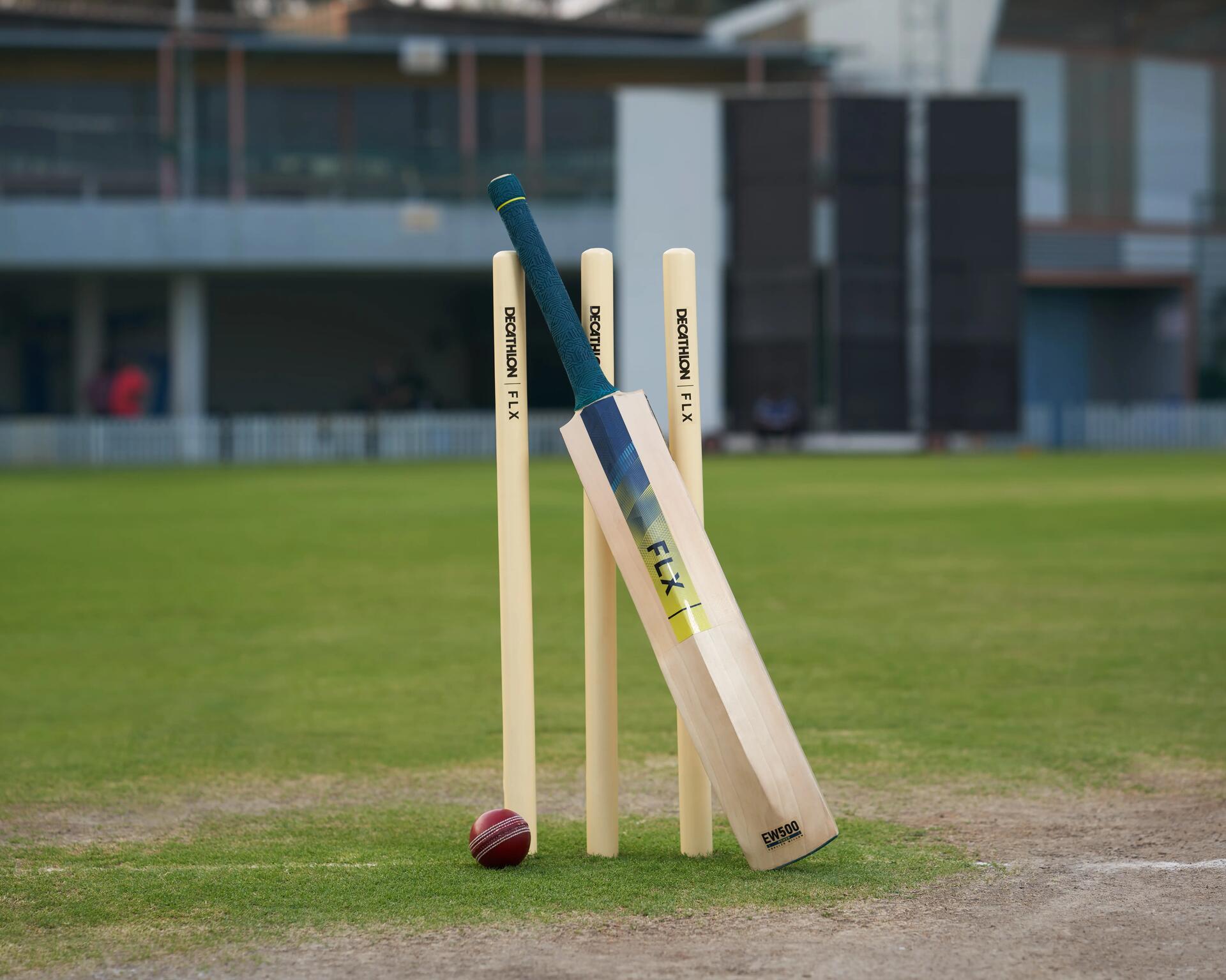 Cricket bat with teal handle leaning up against some wickets