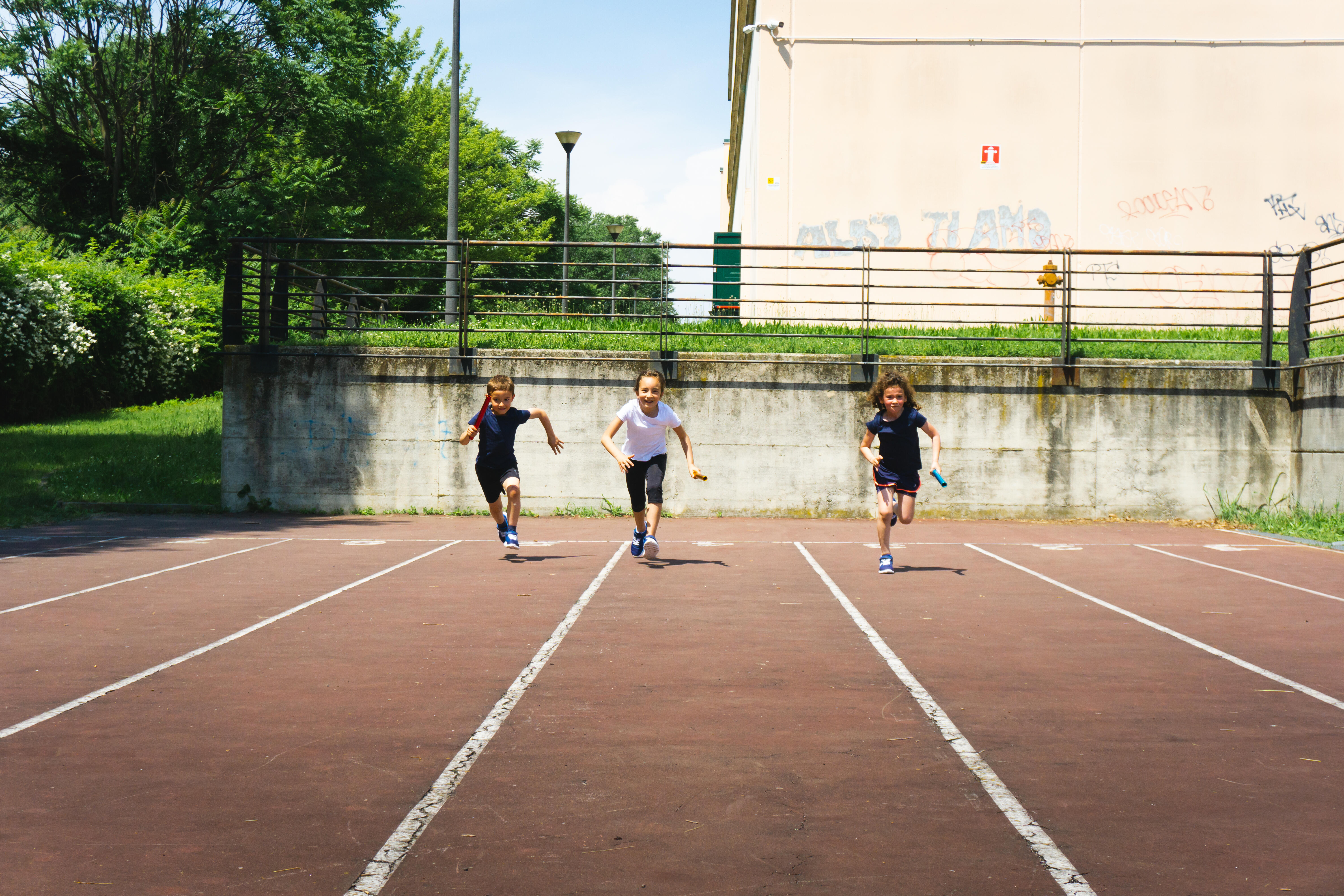 Tre bambine corrono sulla pista di atletica leggera della scuola