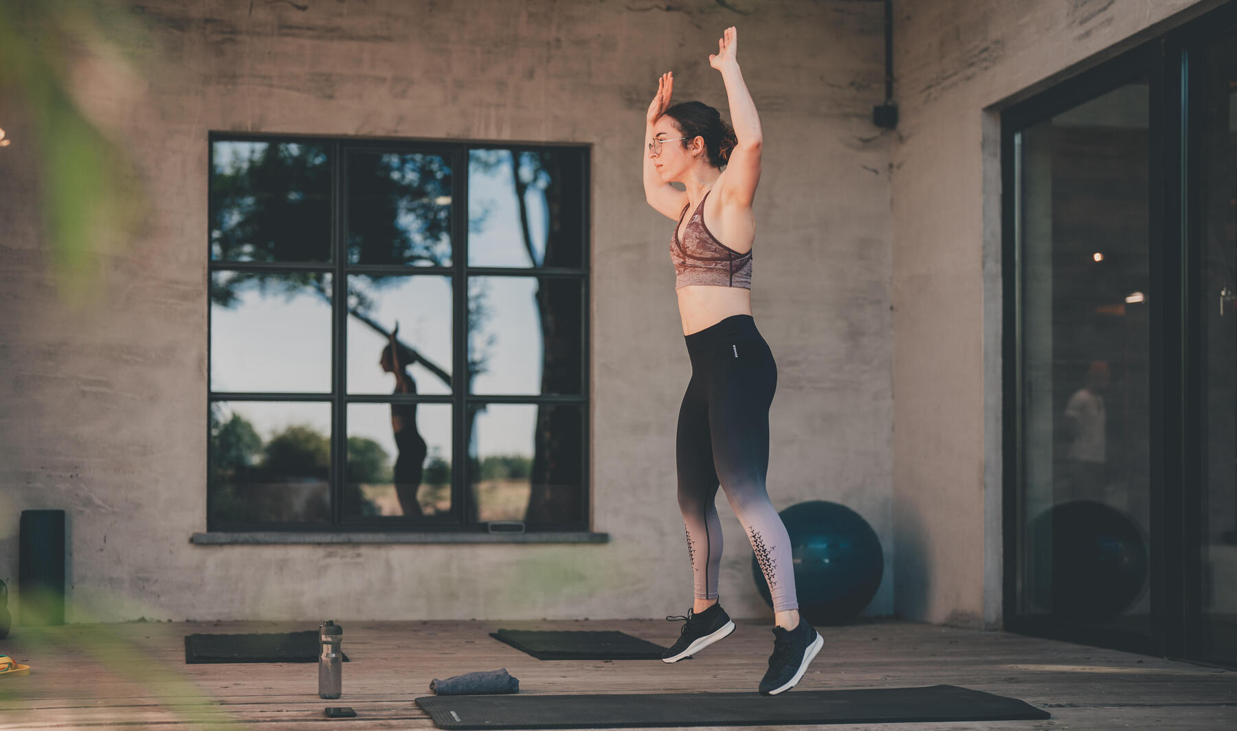 En kvinna i ett gym som är mitt i den uppåtgående rörelsen i burpees.