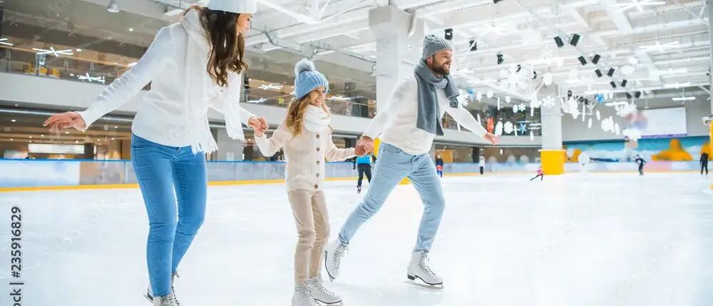 Father, mother and daugher skating in indoor ice rink