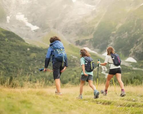A man and two girls hiking in greenery, using nordic walking poles.