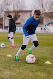 Mladý fotbalista trenující s míčem na hřišti.