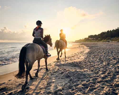 Two people riding a horse on the beach at sunset.