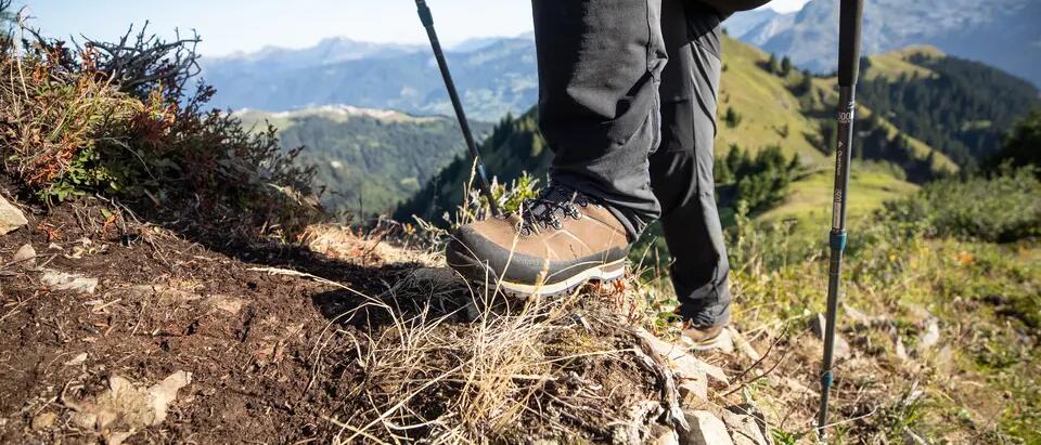 mężczyzna w butach górskich trzymający kijki trekkingowe