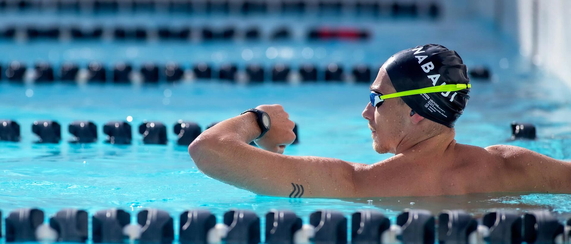 mężczyzna  w czepku na głowie i okularach pływackich patrzący na zegarek 