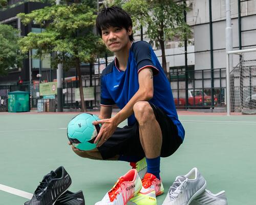 Frau in lila Outfit dribbelt Fußball. Grüner, verschwommener Hintergrund.