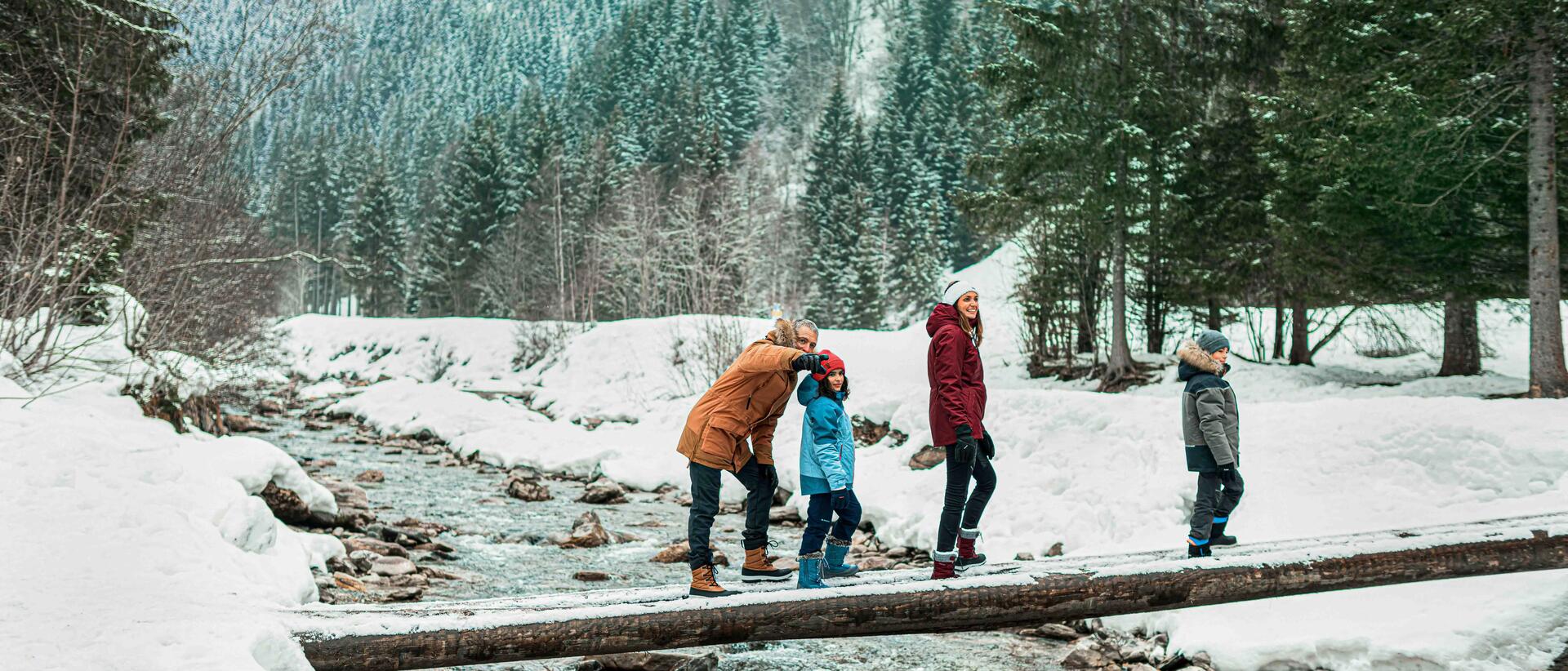 Family walking on a plank of wood, in a forest, covered by snow.