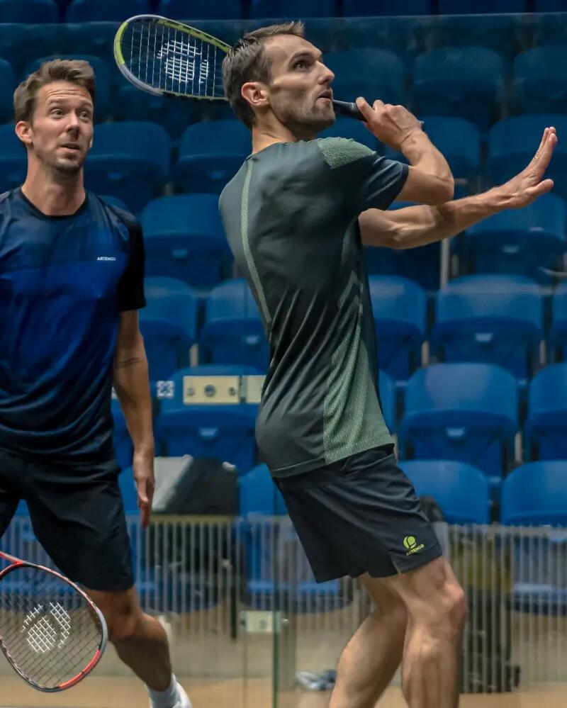 Zewi Männer spielen auf einem Indoor Court Squash, wobei einer der beiden Männer mit einem Squash-Schläger zum Schlag ausholt.