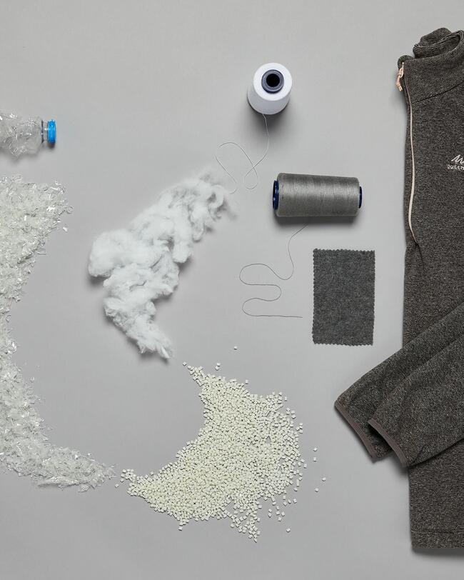Grauer Pullover, Garnrollen, Stoffprobe, recyceltes Plastik, weiße Fasern und Plastikflaschenmaterial auf grauem Hintergrund.
