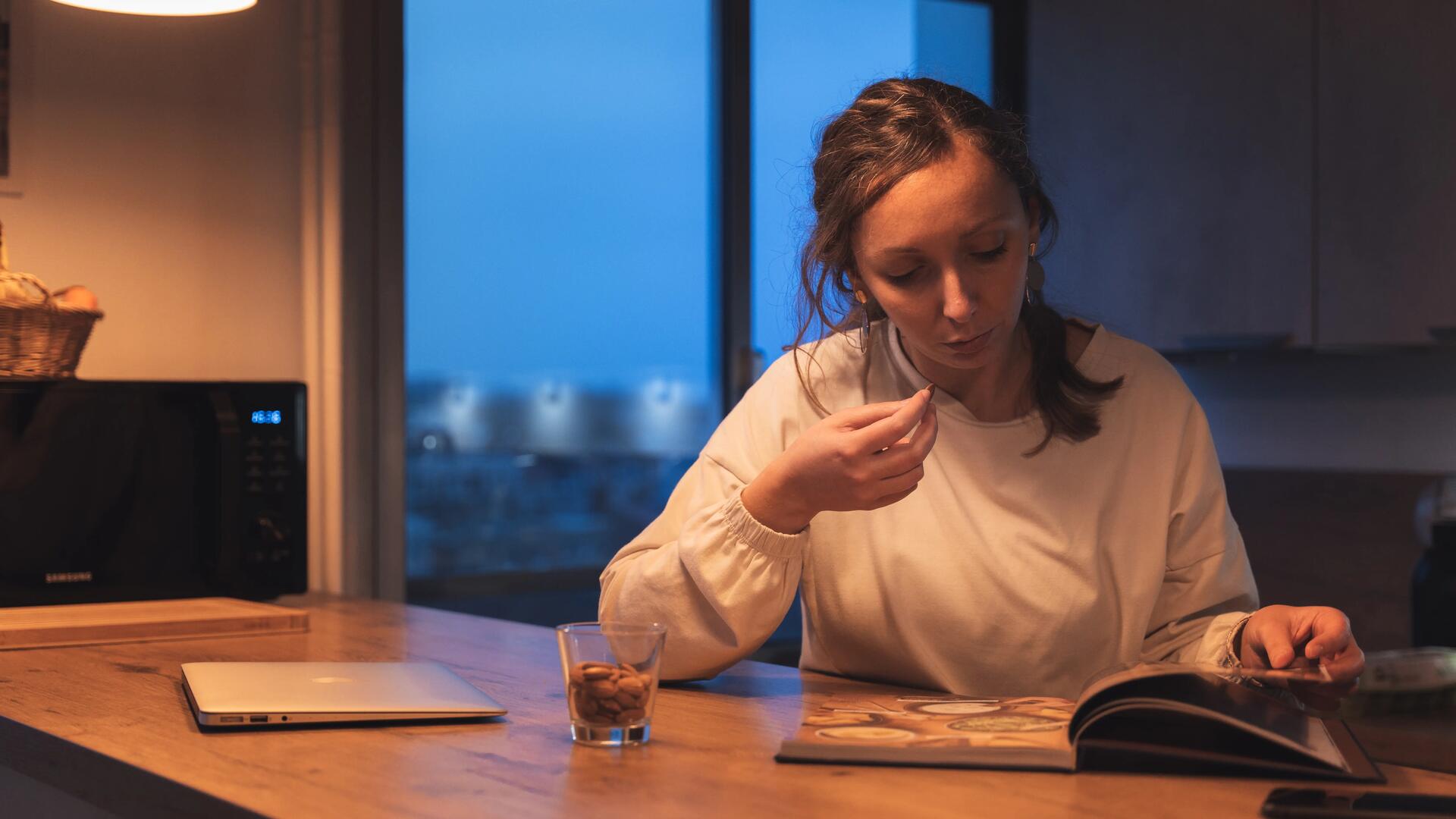 Une femme qui mange des amandes en lisant un bouquin de cuisine