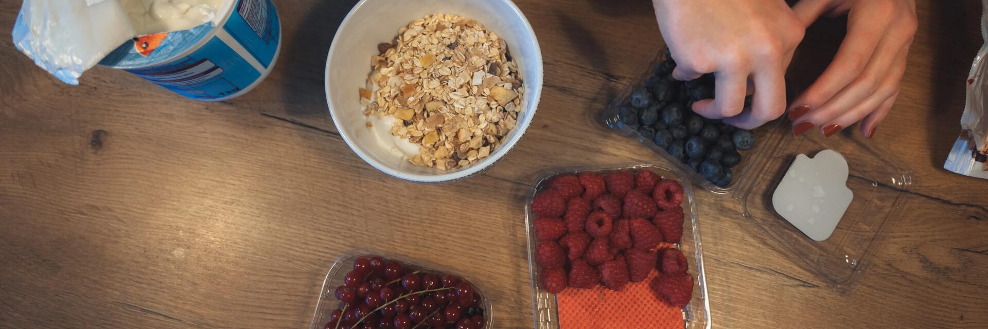 Een tafel met granola, yoghurt, frambozen en bosbessen