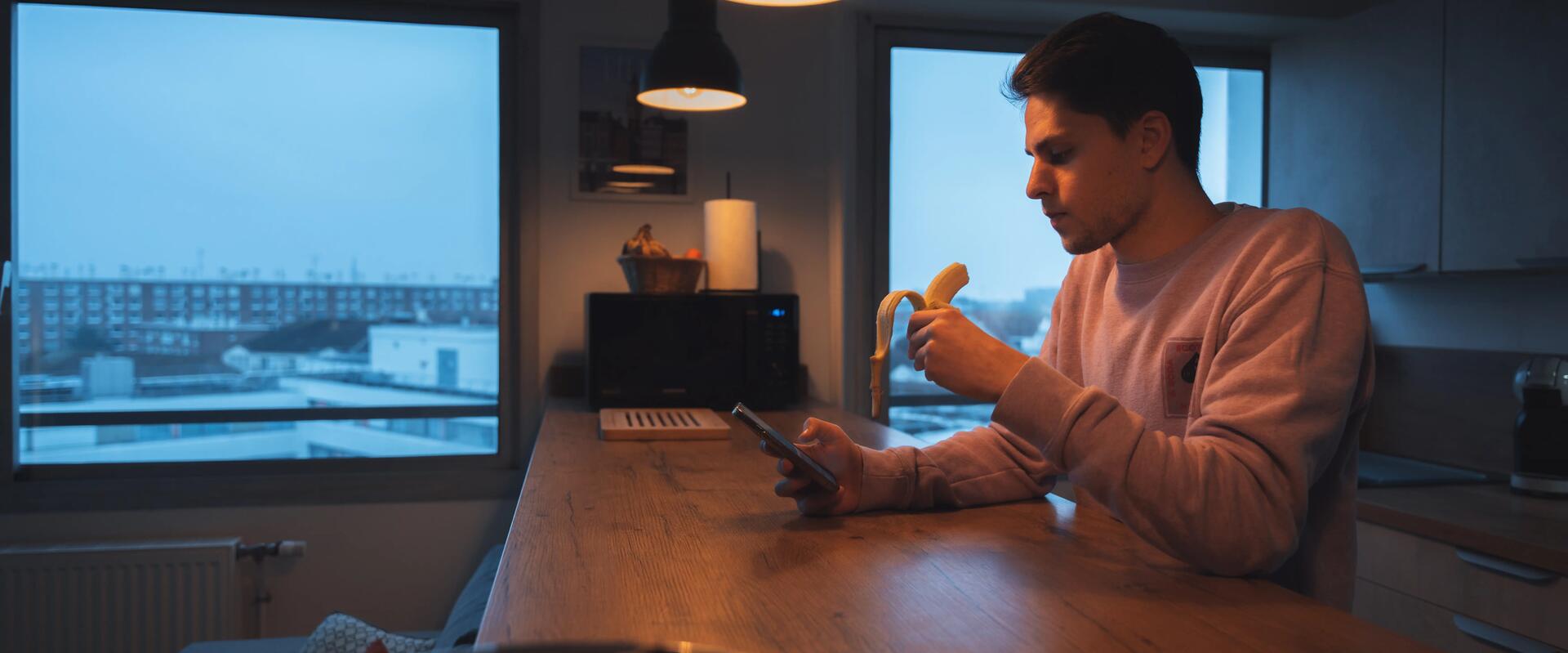 Homme qui mange une banane et consulte son smartphone