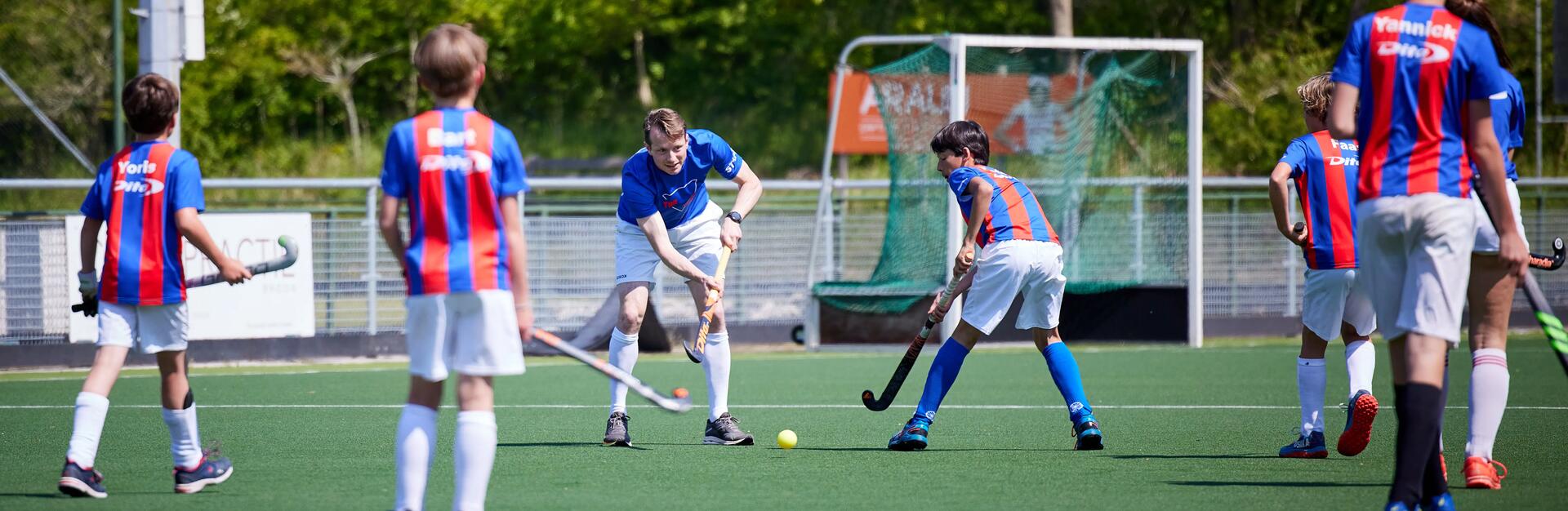 Een groep jonge hockeyspelers op een hockeyveld en hun coach