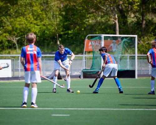 Een groep jonge hockeyspelers op een hockeyveld en hun coach