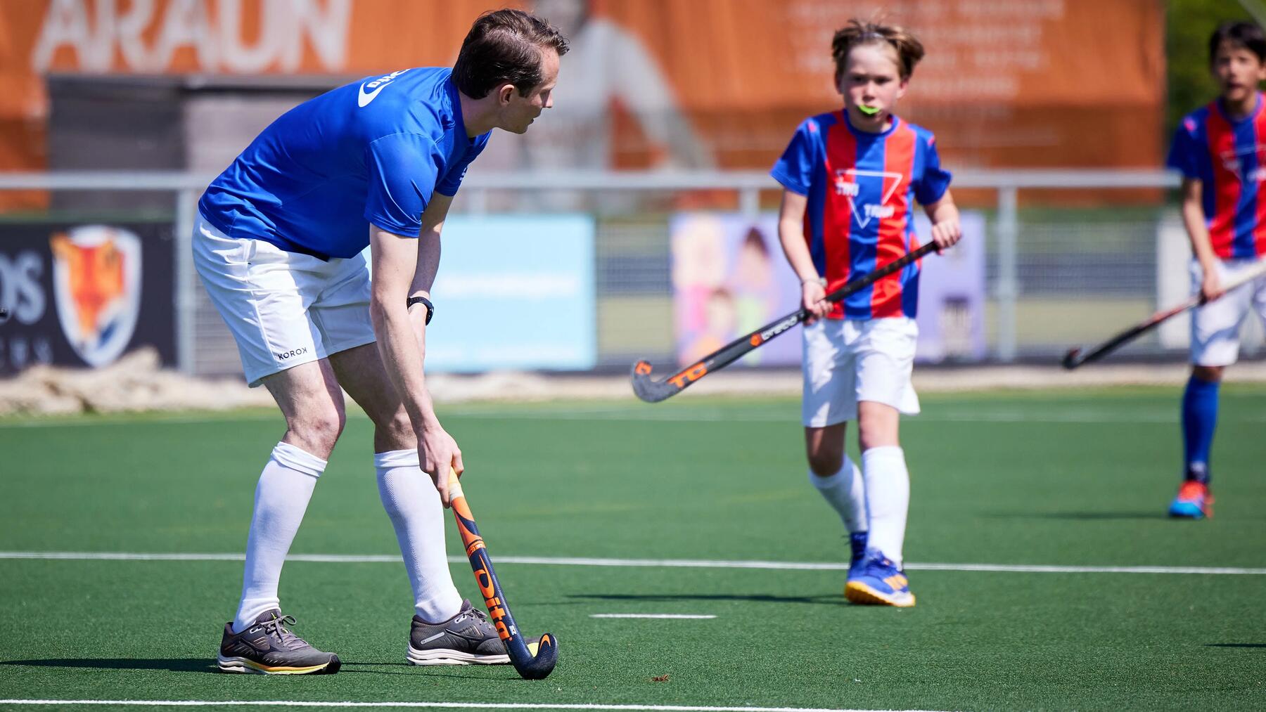 Een coach legt iets uit aan een jonge hockspeler op een hockeyveld