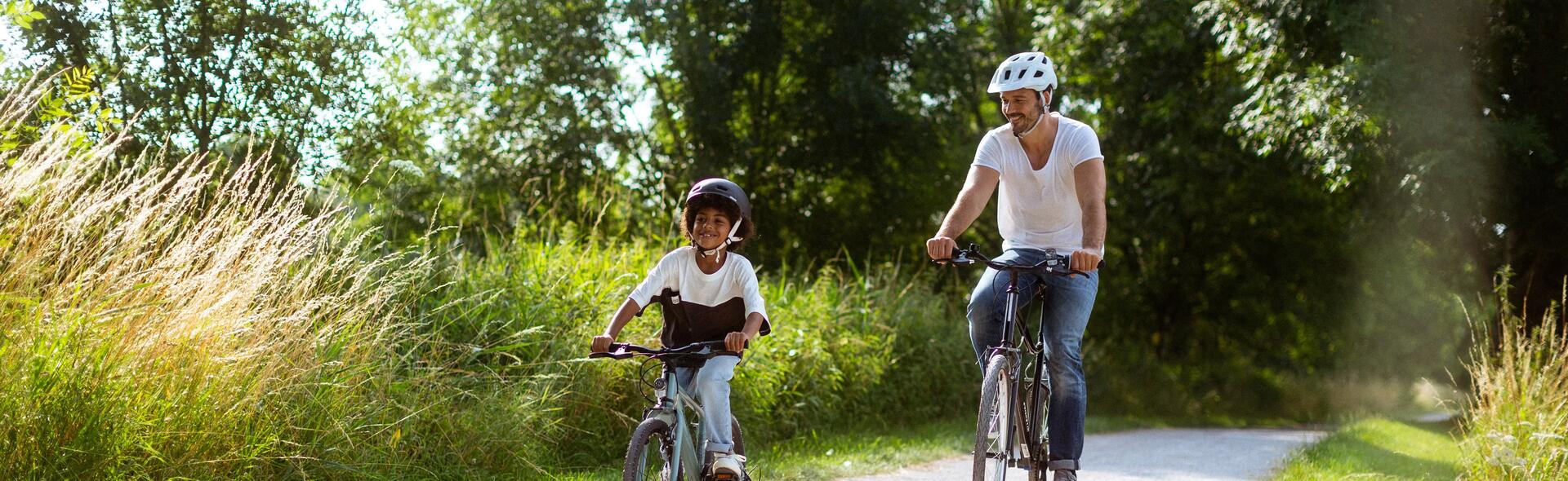 mężczyzna i dziecko jadą na rowerach w kaskach