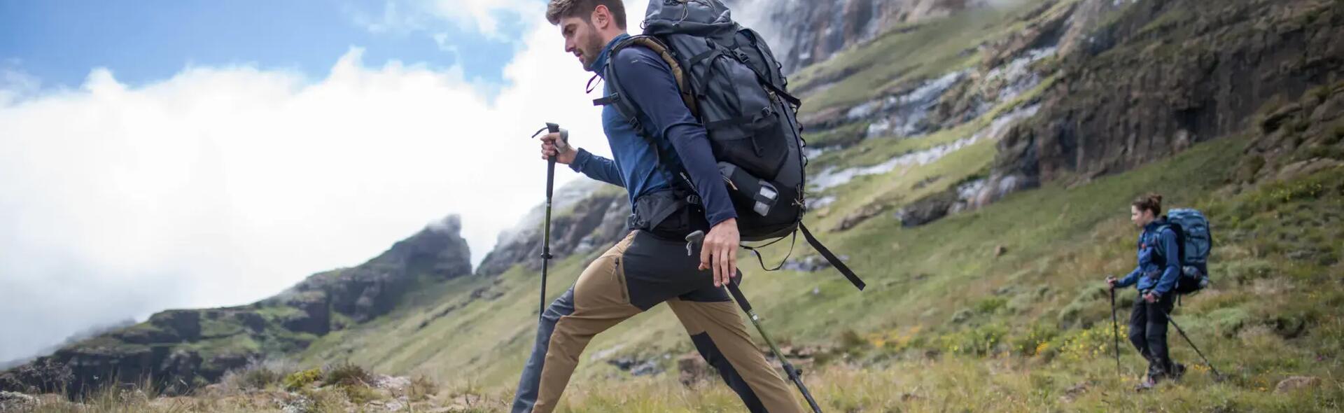 mężczyzna i kobieta wędrujący po górach w odzieży trekkingowej z kijami trekkingowymi i plecakami na plecach