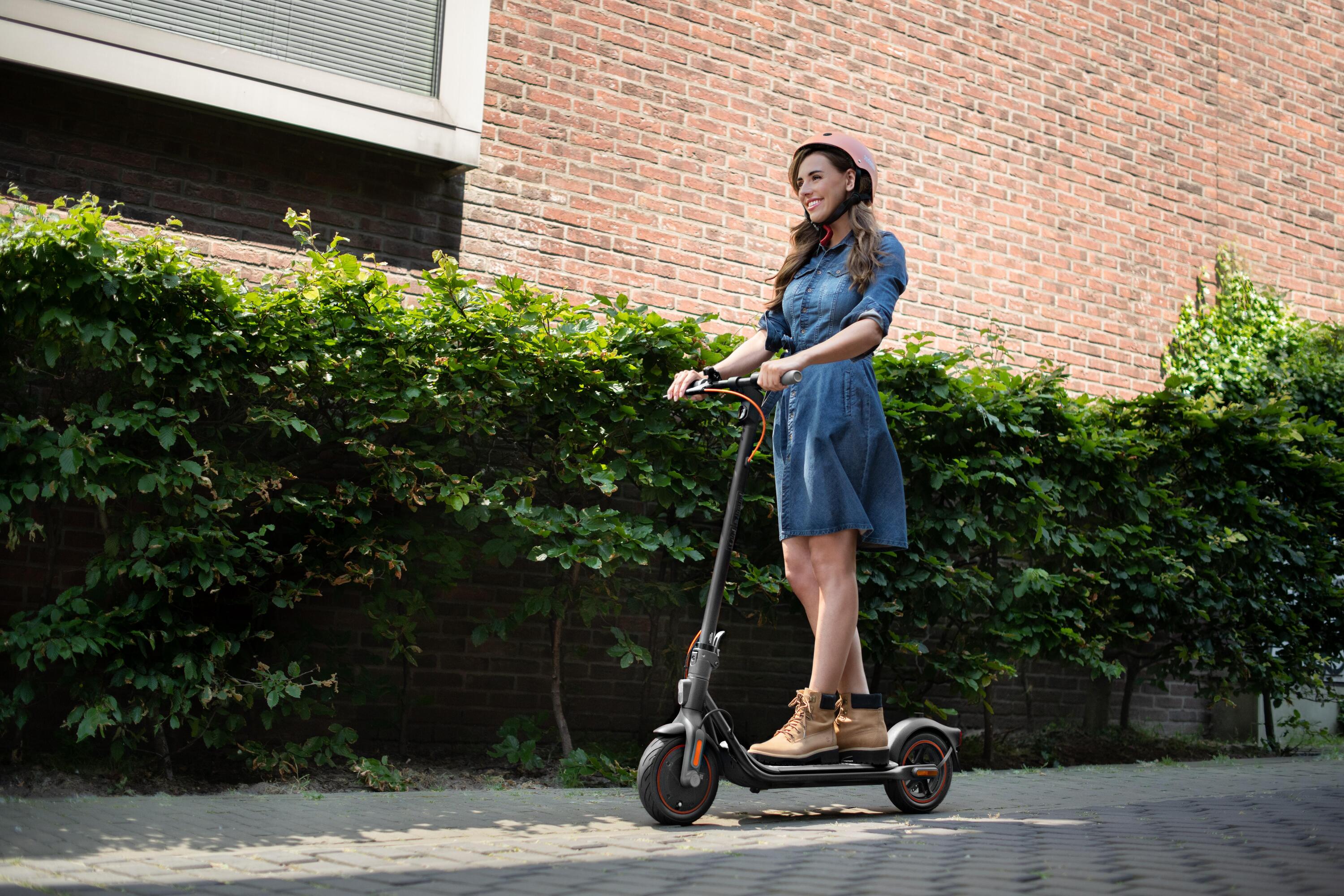 Eine Frau die mit einem E-Scooter über die Straße fährt.